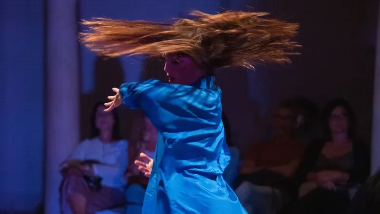 En kvinna i en blå klänning dansar inför publik.
