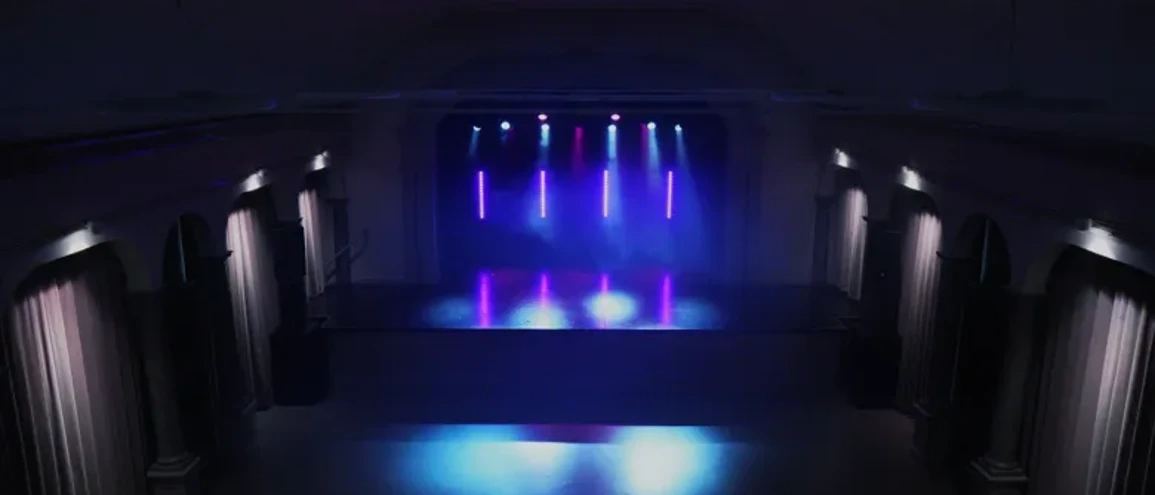 Tom konsertlokal med draperier vid sidorna och blå och rosa belysning.