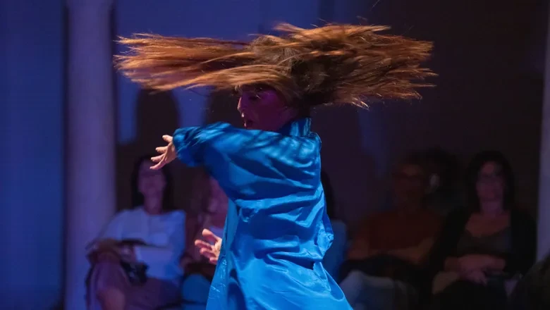 En kvinna i en blå klänning dansar inför publik.