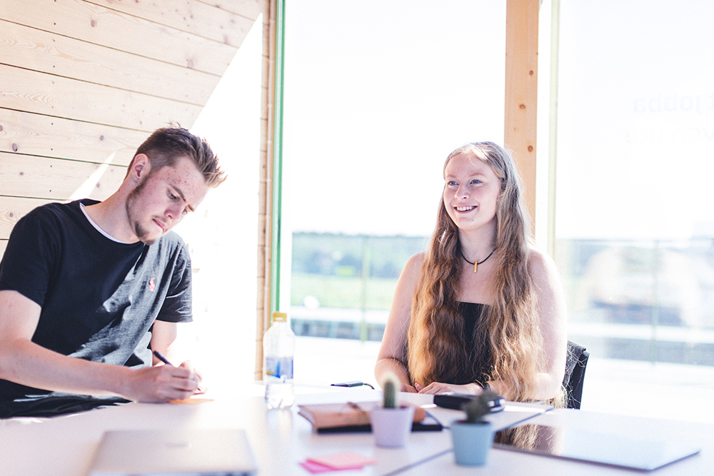 Två unga företagare, en tjej och en kille, sitter vid ett bord och jobbar